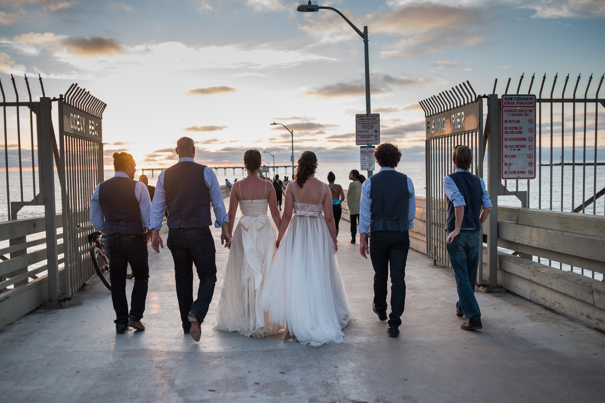 Two brides in Sand Diego walking pier with groomsmen