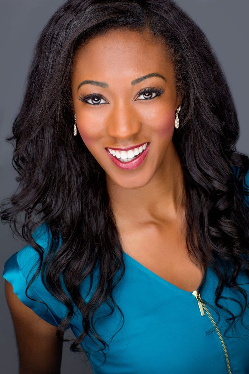 Headshot: curly dark hair, teal top, bright smile