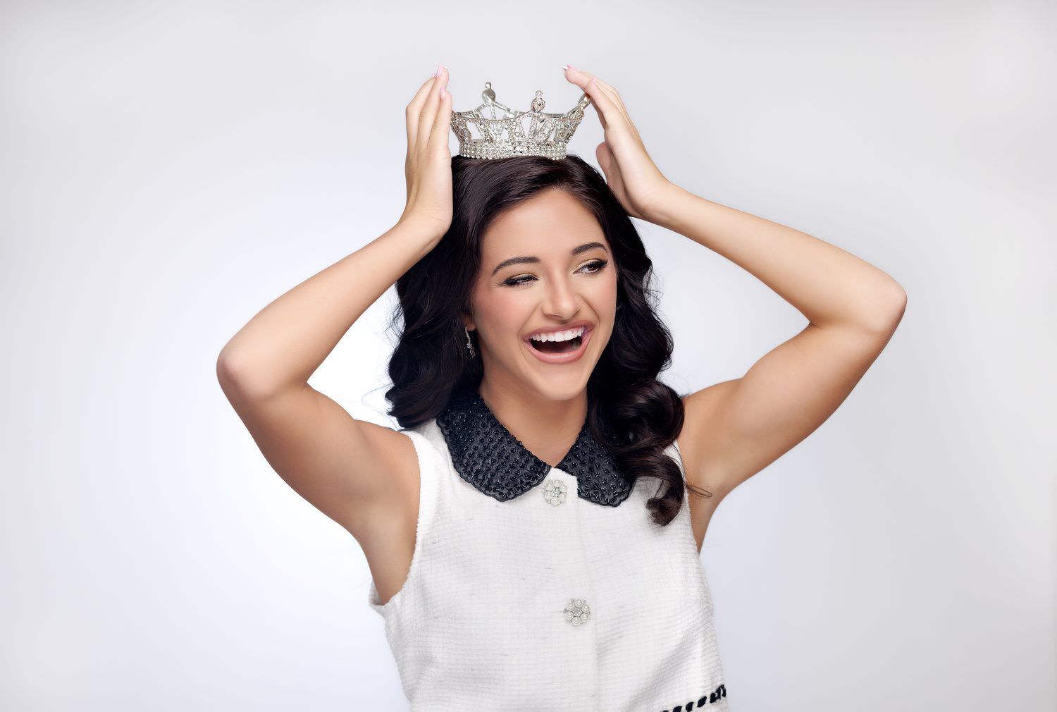 Titleholder laughing with both hands on her crown